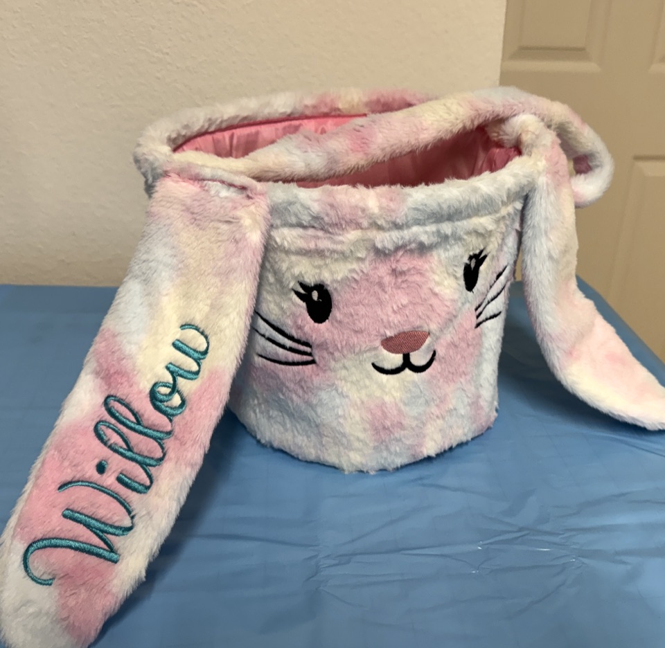 A pink and white plush bunny basket with the name Willow embroidered in teal script down one ear.